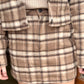 A model showing off a close up view of a brown, khaki, & cream plaid skirt.