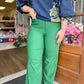 A person standing in a storefront wearing bright green wide-leg pants and a navy blue textured blouse with a yellow and green floral pattern. The photo is cropped from the shoulders down, showing the pants and lower torso. 
