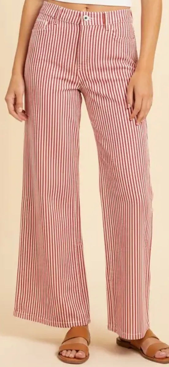 A person wearing wide-leg pants with vertical red and white stripes, paired with tan slide sandals, against a plain beige studio background.
