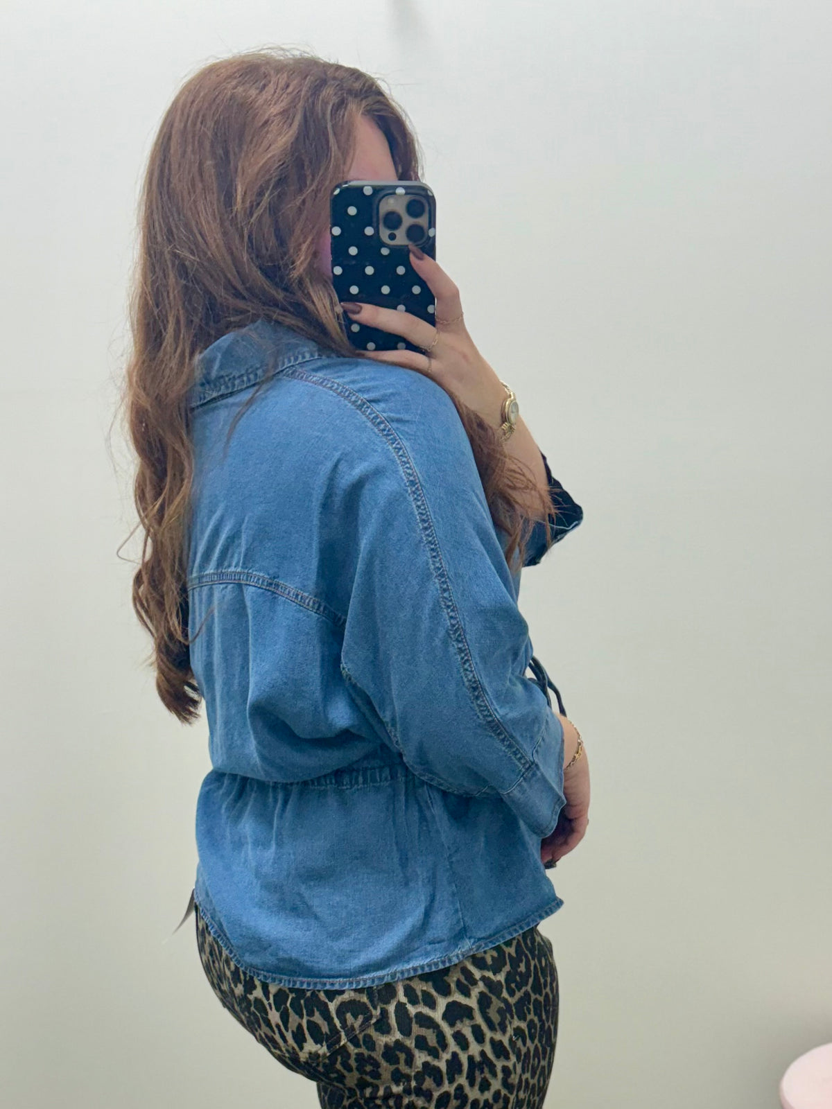 A woman taking a mirror selfie wearing a light blue denim top and leopard print pants, showing off the side view of the outfit.