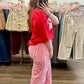 A woman takes a mirror selfie in a clothing boutique, wearing a bright red oversized t-shirt and red and white vertically striped wide-leg pants.