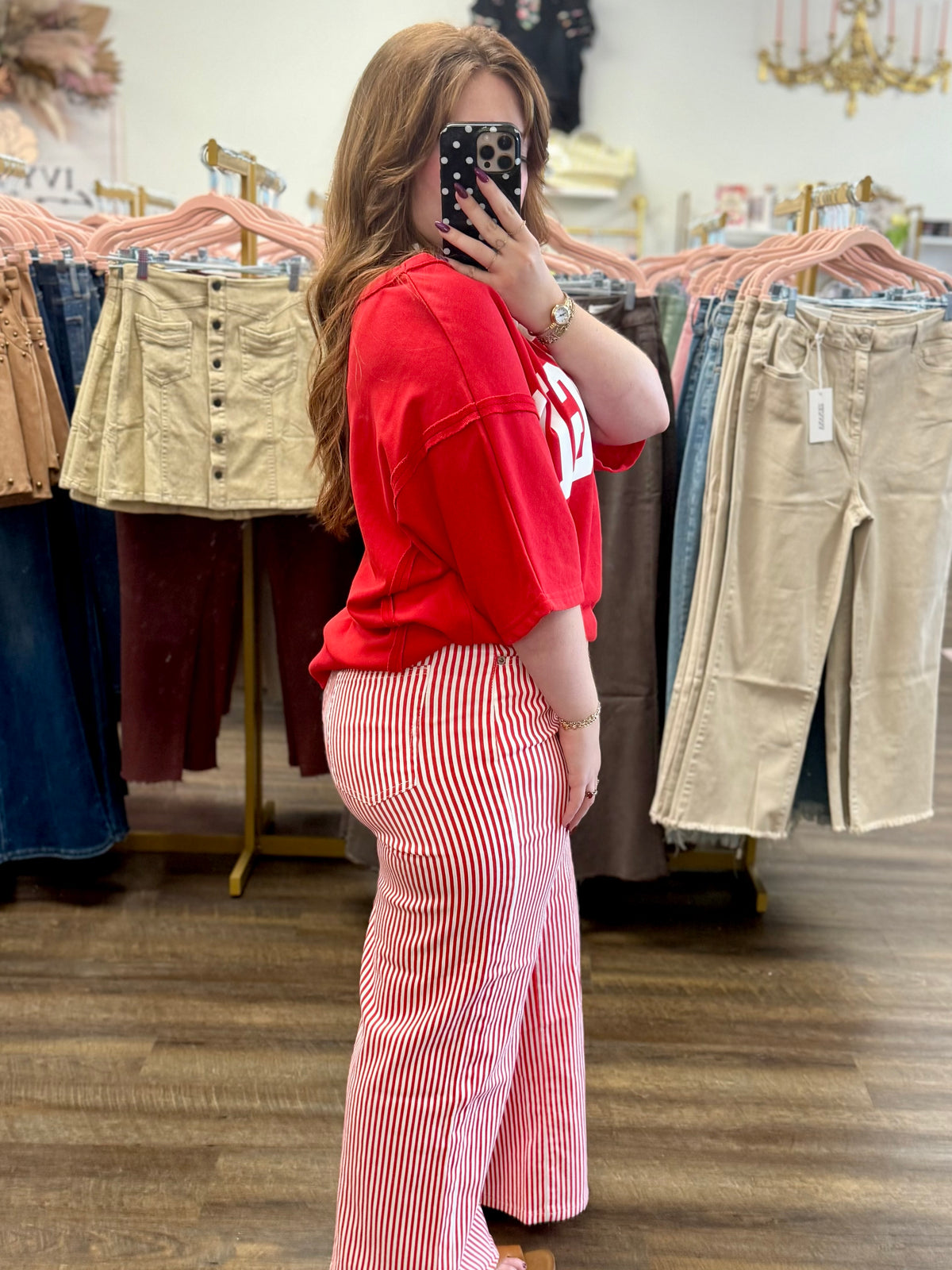 A woman takes a mirror selfie in a clothing boutique, wearing a bright red oversized t-shirt and red and white vertically striped wide-leg pants.