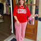 A woman stands in a doorway wearing a bright red oversized sweatshirt with 'GEORGIA' printed in white across the front, paired with red and white vertically striped wide-leg pants.
