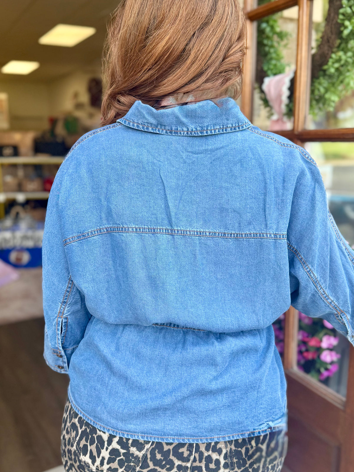 A person viewed from behind wearing a light blue denim top paired with leopard jeans, standing in a store interior.