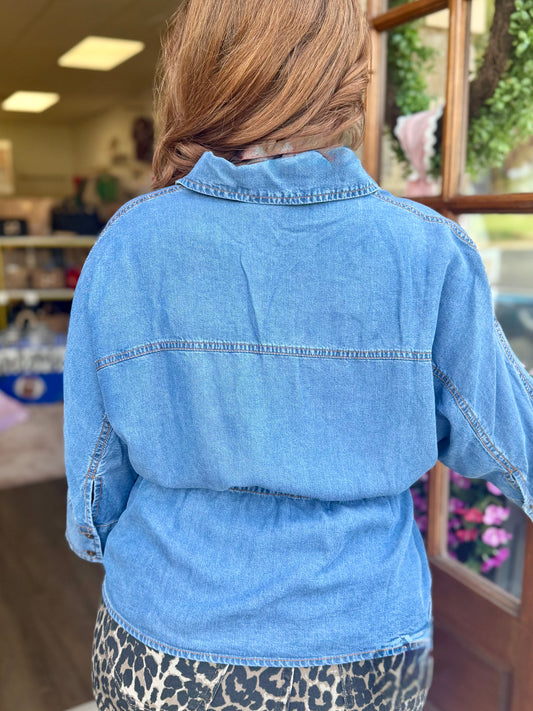 A person viewed from behind wearing a light blue denim top paired with leopard jeans, standing in a store interior.
