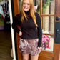A woman wearing a black ribbed mock-neck sweater and a brown and white patterned mini skirt, paired with brown boots.