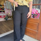 A person wearing black wide-leg pants and a yellow cardigan stands in a storefront doorway. The photo is cropped from the shoulders down, showing off the pants fit. 