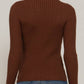 A woman shown from the back wearing a brown ribbed mock neck long-sleeve sweater and blue jeans against a plain light background.