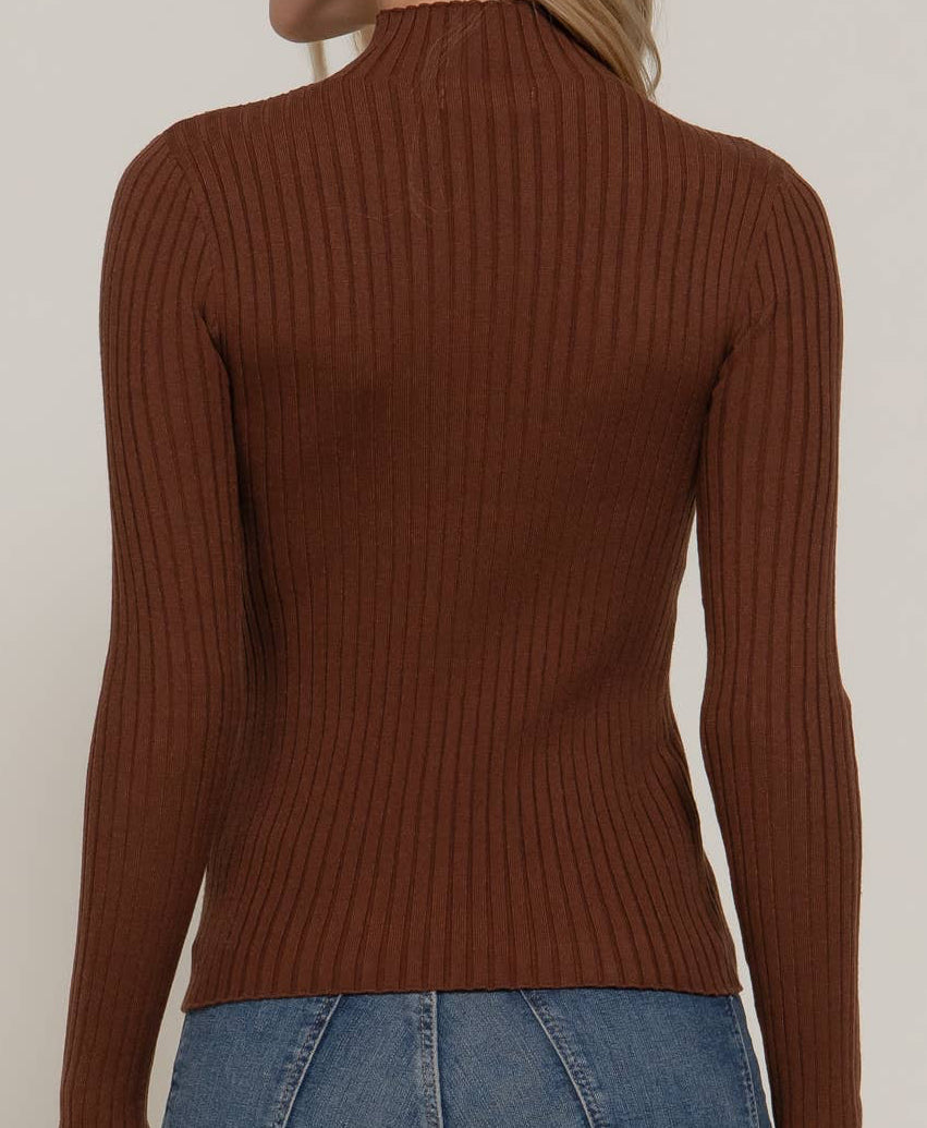 A woman shown from the back wearing a brown ribbed mock neck long-sleeve sweater and blue jeans against a plain light background.