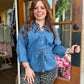 A woman stands in a doorway wearing a blue denim long-sleeve top with a drawstring waist and a patterned scarf, paired with leopard-print pants.