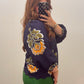 A woman taking a mirror selfie wearing a navy blue textured blouse with yellow and green floral embroidery on the sleeves and bodice, paired with green pants.