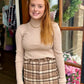 A woman modeling a beige ribbed fitted sweater paired with a matching plaid skirt.