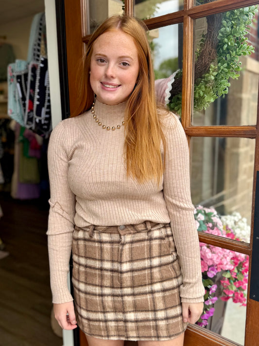 A woman modeling a beige ribbed fitted sweater paired with a matching plaid skirt.