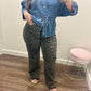 A person taking a mirror selfie wearing a blue denim shirt and wide-leg leopard print pants.